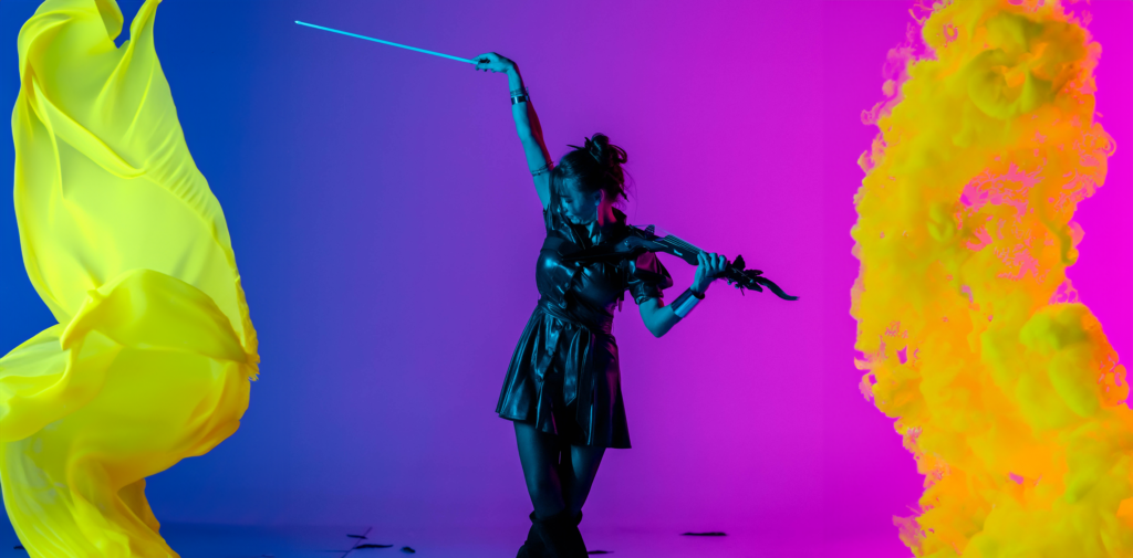 A woman in a black dress plays the violin on a purple and blue-lit stage, with vibrant yellow and orange flowing shapes on either side of her.