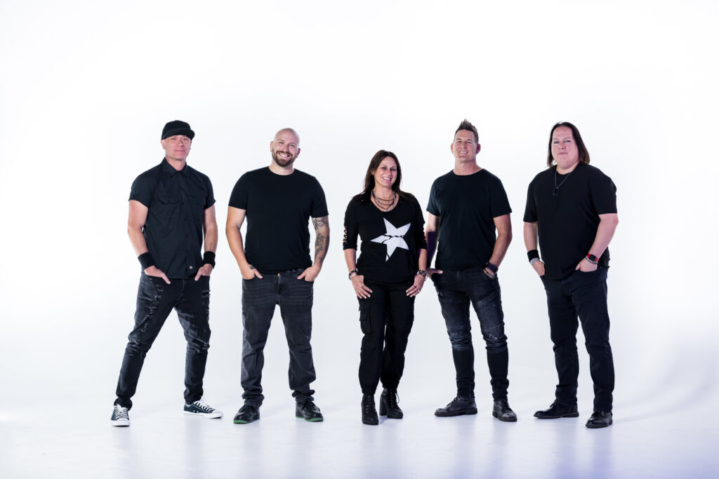Five people stand in a row against a white background, all dressed in black outfits. The group consists of four men and one woman, all facing the camera and smiling slightly.