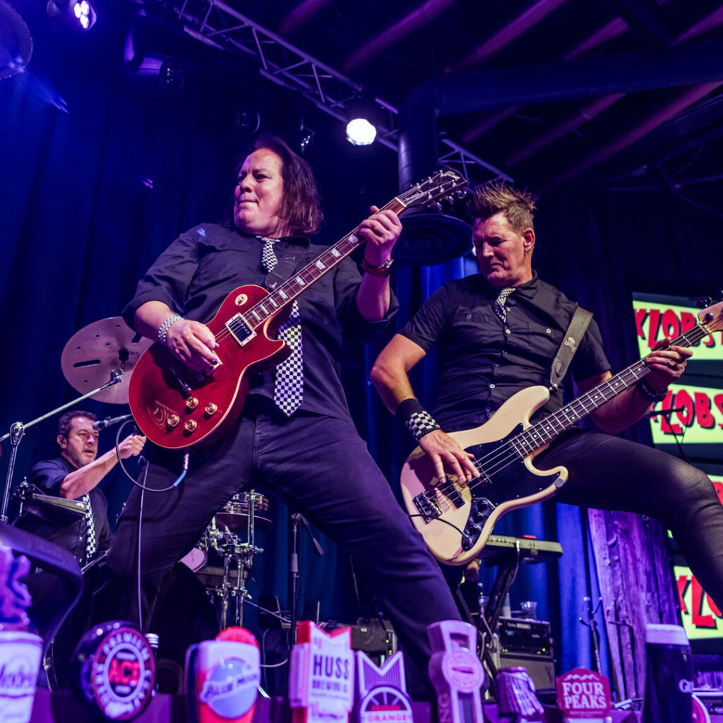 image of two guitarists jamming on stage with a drummer in the background